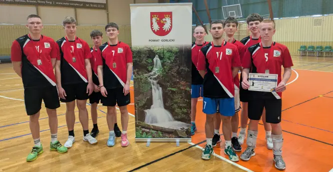 Drużyna siatkarzy pozująca z dyplomem i banerem Powiatu